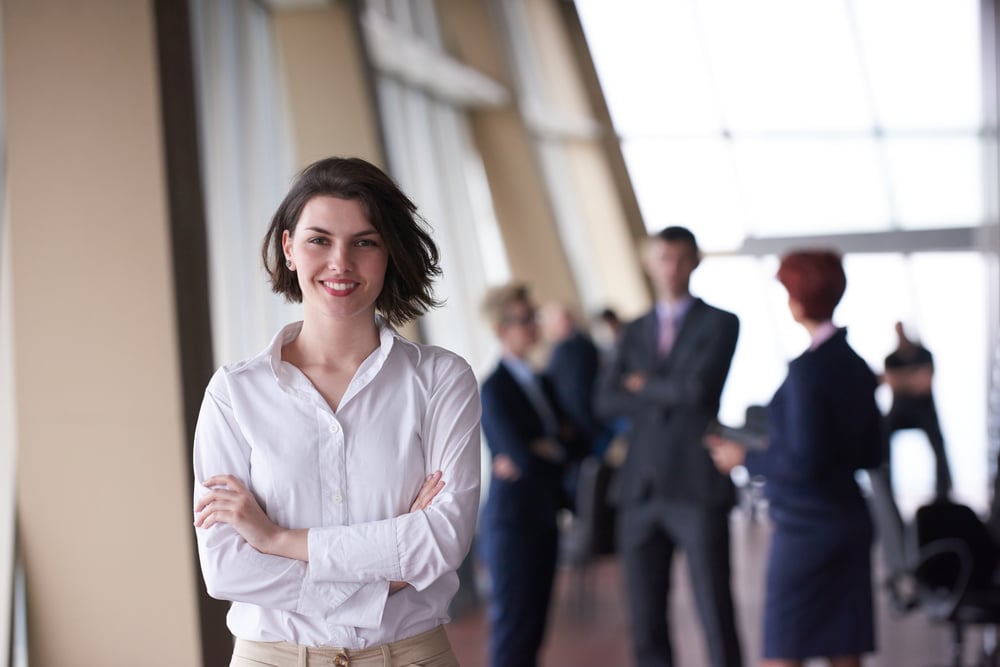 Smilling young business woman in front her team blured in background. Group of young business people. Modern bright startup office interior.